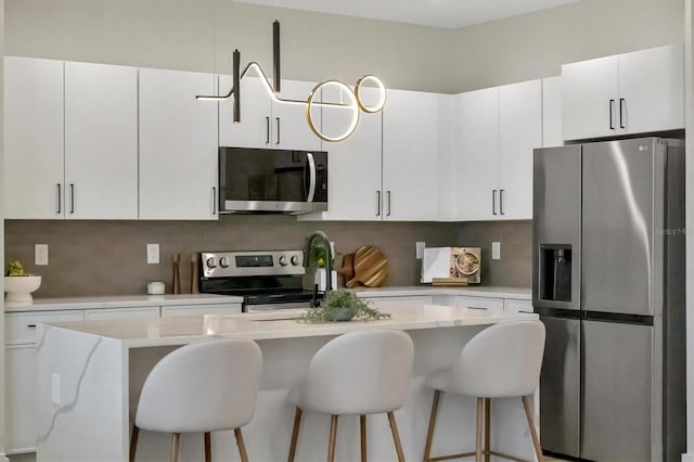 kitchen with a kitchen bar, backsplash, stainless steel appliances, a center island, and white cabinetry