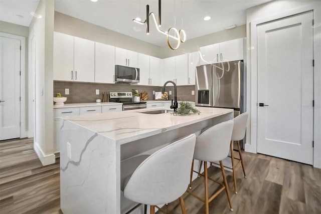 kitchen featuring stainless steel appliances, a kitchen island with sink, sink, decorative light fixtures, and white cabinets