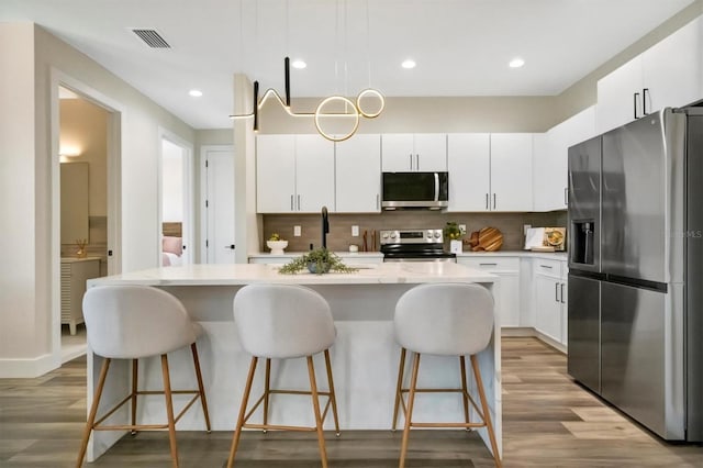 kitchen featuring decorative backsplash, appliances with stainless steel finishes, light hardwood / wood-style flooring, white cabinets, and a kitchen island