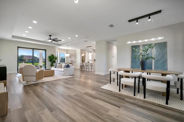 interior space with ceiling fan, a tray ceiling, and light hardwood / wood-style flooring