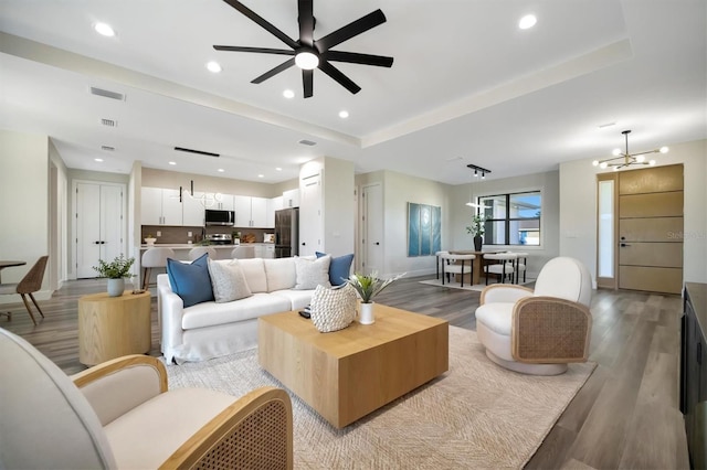 living room featuring ceiling fan with notable chandelier, light wood-type flooring, and a raised ceiling