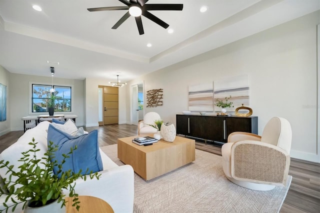 living room featuring a tray ceiling, hardwood / wood-style floors, and ceiling fan with notable chandelier