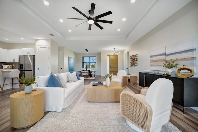 living room with light hardwood / wood-style floors, ceiling fan, and a tray ceiling