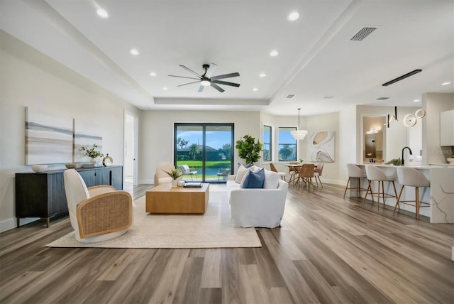 living room with ceiling fan, a raised ceiling, wood-type flooring, and sink