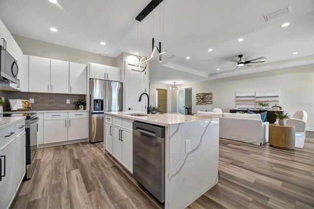 kitchen with a kitchen island with sink, sink, light hardwood / wood-style flooring, appliances with stainless steel finishes, and white cabinetry