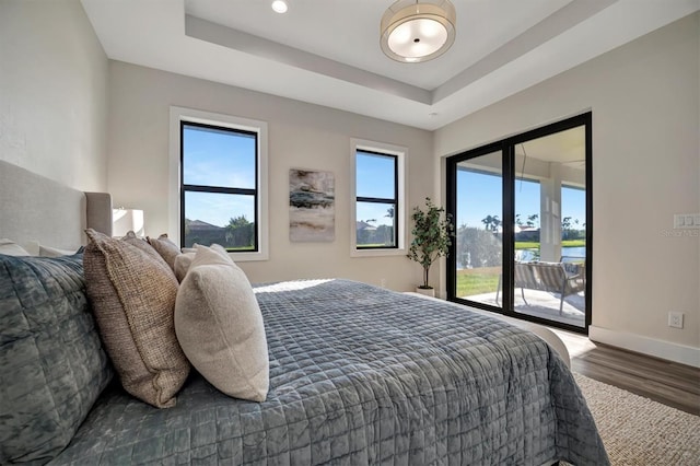 bedroom featuring hardwood / wood-style flooring, a raised ceiling, a water view, and access to exterior