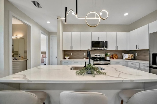 kitchen featuring appliances with stainless steel finishes, backsplash, a breakfast bar, sink, and white cabinets