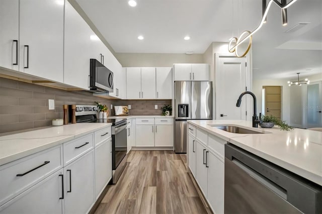 kitchen featuring stainless steel appliances, sink, decorative light fixtures, white cabinets, and light hardwood / wood-style floors