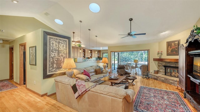 living room with ceiling fan, light hardwood / wood-style floors, a stone fireplace, and lofted ceiling