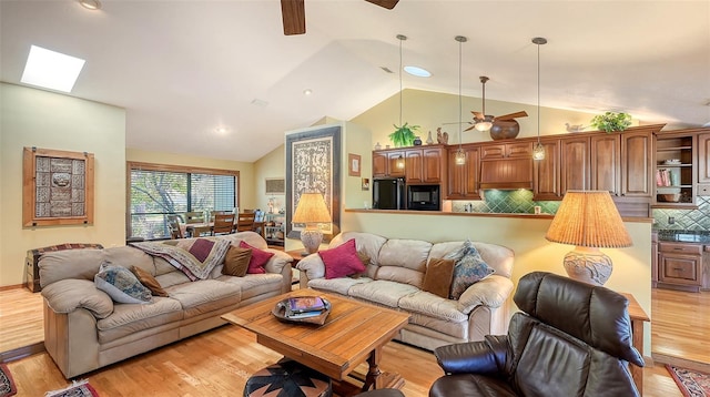 living room featuring lofted ceiling with skylight, ceiling fan, and light hardwood / wood-style floors