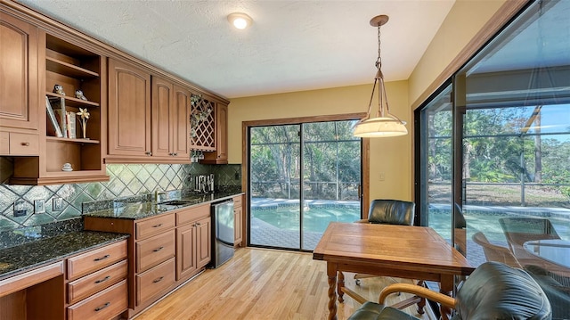 kitchen with sink, decorative backsplash, light wood-type flooring, black dishwasher, and decorative light fixtures