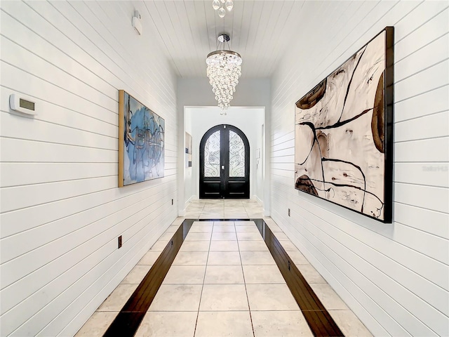 doorway featuring french doors, light tile patterned floors, brick wall, and a notable chandelier