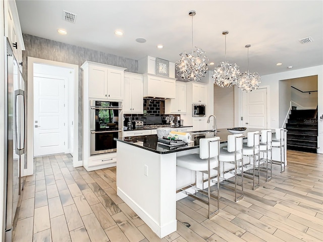 kitchen with stainless steel appliances, pendant lighting, a chandelier, white cabinetry, and an island with sink