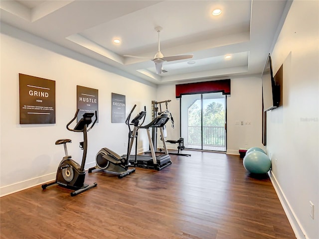 workout room featuring ceiling fan, dark wood-type flooring, and a tray ceiling