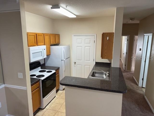 kitchen with white appliances, light carpet, sink, a textured ceiling, and kitchen peninsula