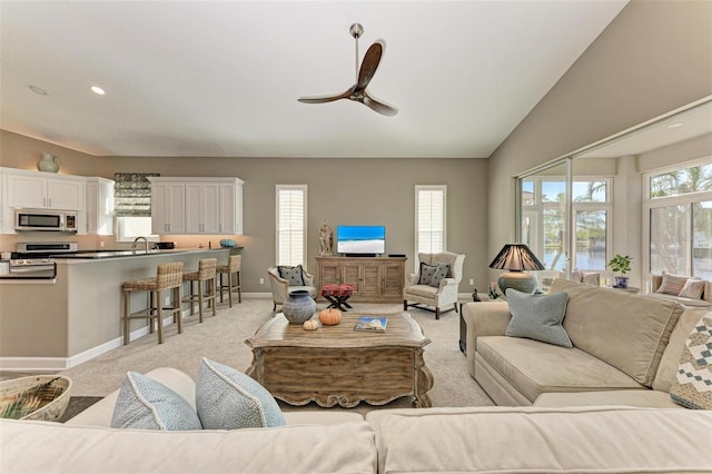 carpeted living room with ceiling fan, sink, and vaulted ceiling