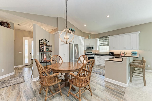 dining room featuring light wood-type flooring, lofted ceiling, sink, and a chandelier