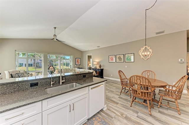 kitchen featuring dishwasher, sink, dark stone counters, lofted ceiling, and white cabinets