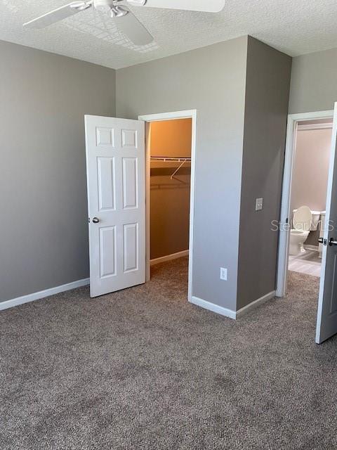 unfurnished bedroom featuring carpet flooring, a walk in closet, a textured ceiling, ceiling fan, and a closet