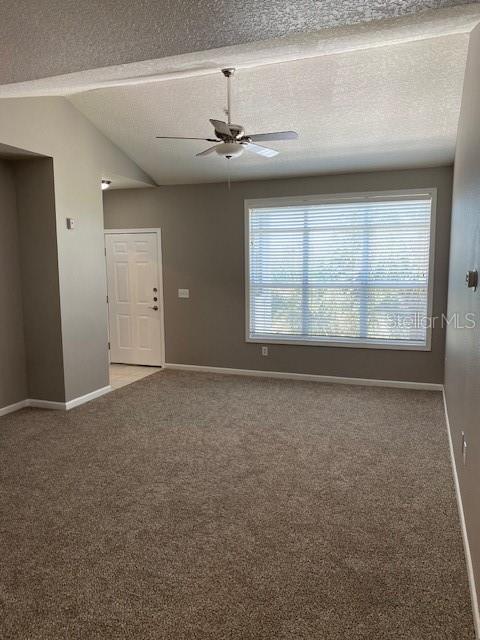 carpeted spare room featuring a textured ceiling, ceiling fan, and lofted ceiling