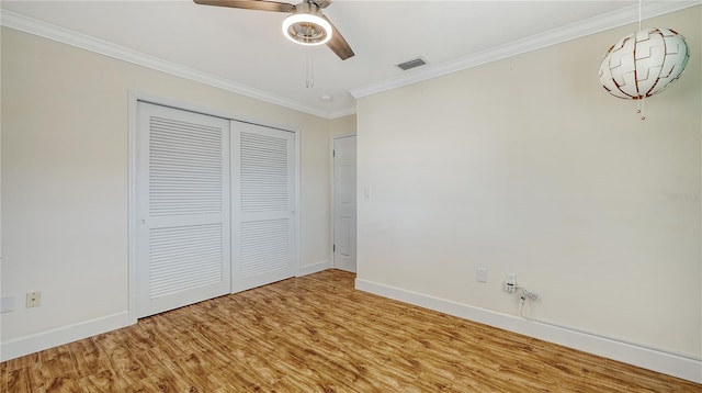 unfurnished bedroom with crown molding, a closet, visible vents, wood finished floors, and baseboards