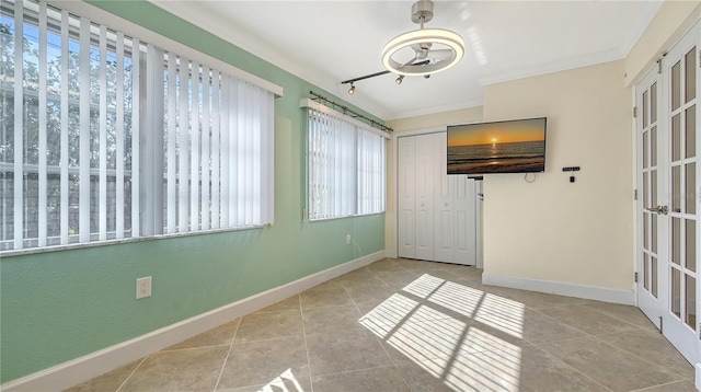 unfurnished room with light tile patterned floors, baseboards, ornamental molding, rail lighting, and french doors