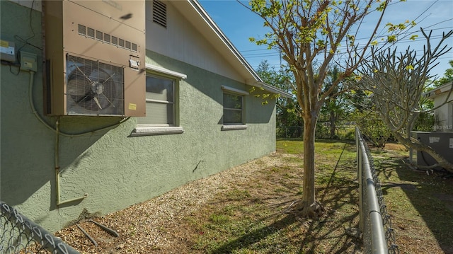 view of side of property with ac unit, fence, central AC unit, and stucco siding