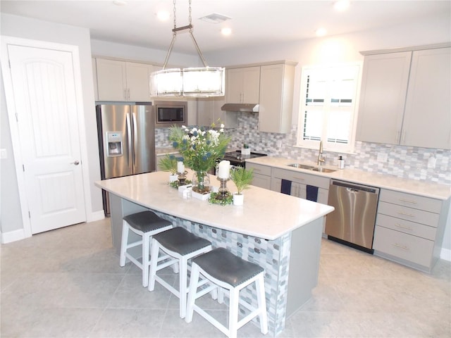 kitchen with gray cabinets, a kitchen island, appliances with stainless steel finishes, pendant lighting, and sink