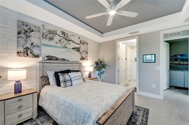 bedroom featuring ceiling fan, washing machine and dryer, ensuite bathroom, a raised ceiling, and wood walls