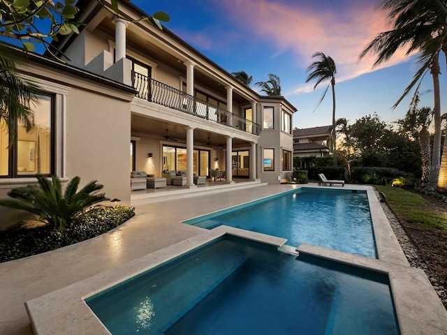 pool at dusk with an in ground hot tub, ceiling fan, a patio, and an outdoor living space