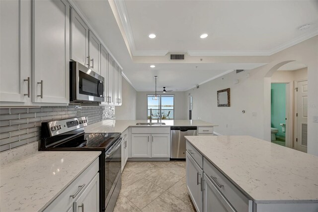 kitchen featuring kitchen peninsula, appliances with stainless steel finishes, decorative backsplash, light stone countertops, and ornamental molding