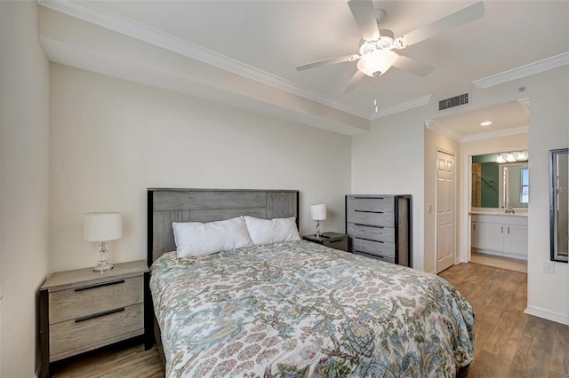 bedroom featuring ceiling fan, light wood-type flooring, crown molding, and ensuite bath