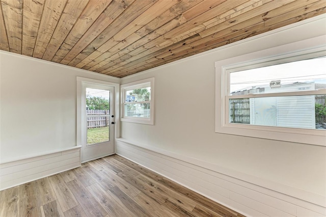 empty room featuring wood walls, light hardwood / wood-style flooring, wooden ceiling, and ornamental molding