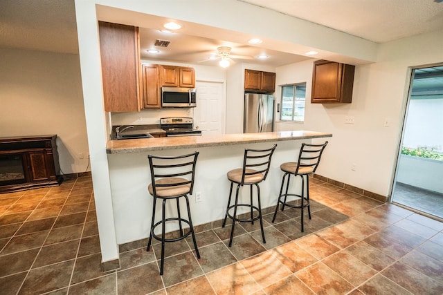 kitchen featuring sink, ceiling fan, appliances with stainless steel finishes, a kitchen bar, and kitchen peninsula