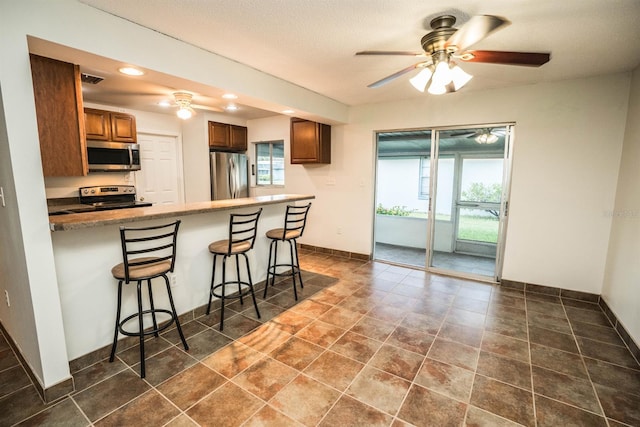 kitchen with kitchen peninsula, stainless steel appliances, dark tile patterned floors, ceiling fan, and a breakfast bar area