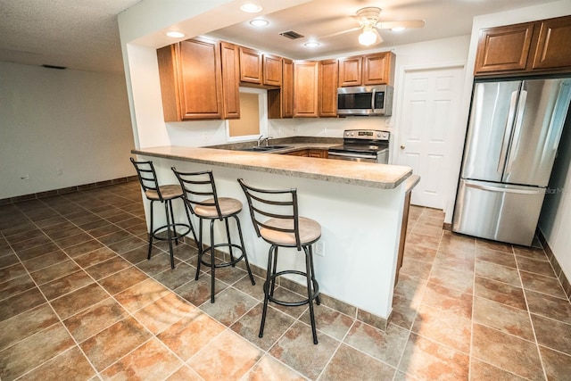 kitchen featuring a kitchen bar, kitchen peninsula, stainless steel appliances, ceiling fan, and sink