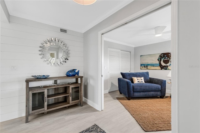 living area featuring ceiling fan, wooden walls, ornamental molding, and hardwood / wood-style flooring