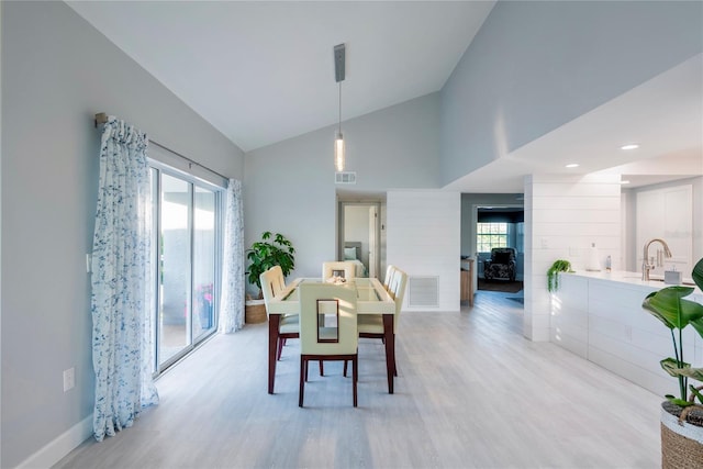 dining area with high vaulted ceiling, light hardwood / wood-style floors, sink, and a wealth of natural light