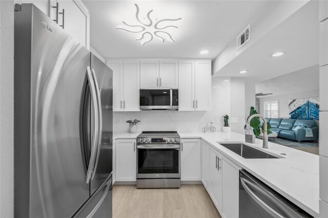 kitchen with white cabinetry, sink, tasteful backsplash, light hardwood / wood-style flooring, and appliances with stainless steel finishes