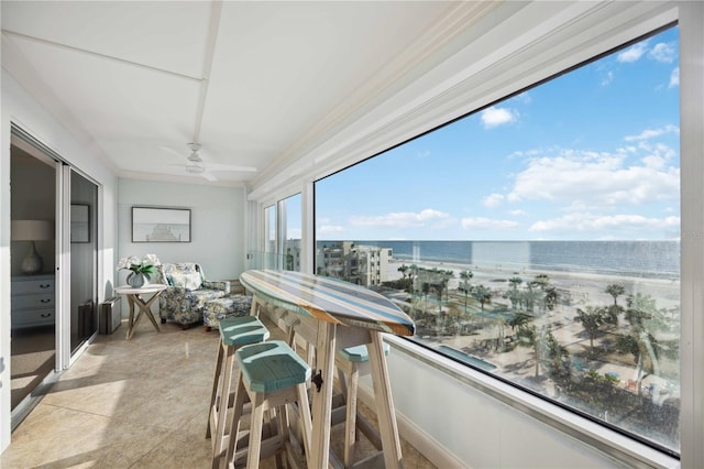 sunroom / solarium with a water view, ceiling fan, and a view of the beach