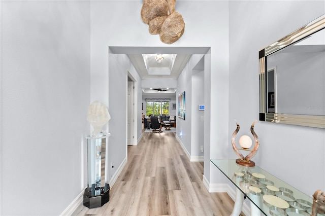 corridor featuring light wood-type flooring, ornamental molding, and a tray ceiling