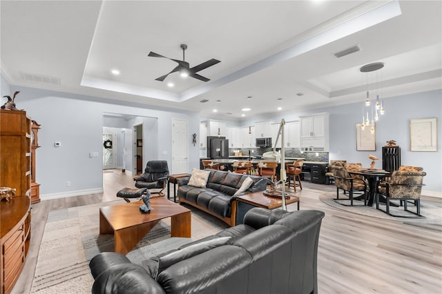 living room featuring a tray ceiling, ceiling fan, ornamental molding, and light wood-type flooring