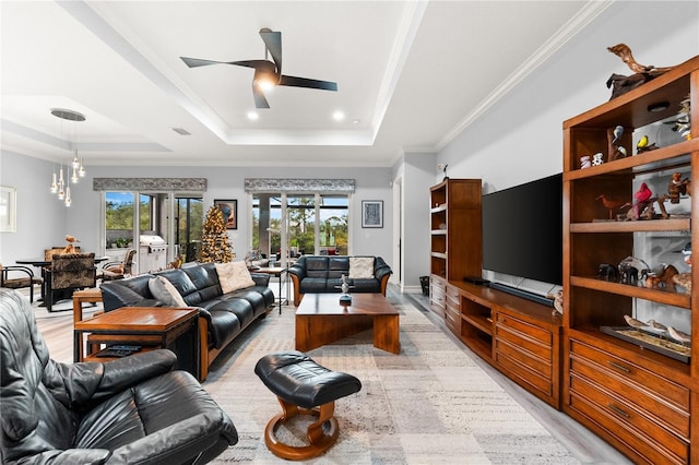 living room featuring french doors, a raised ceiling, light wood-type flooring, ceiling fan with notable chandelier, and ornamental molding