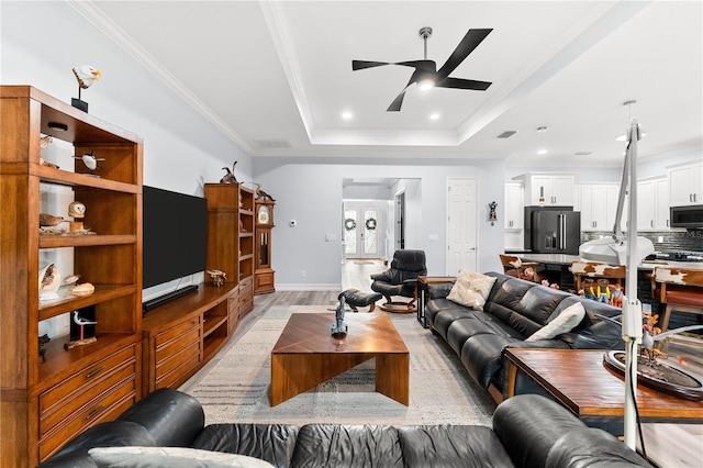 living room featuring a tray ceiling, ceiling fan, light hardwood / wood-style flooring, and ornamental molding