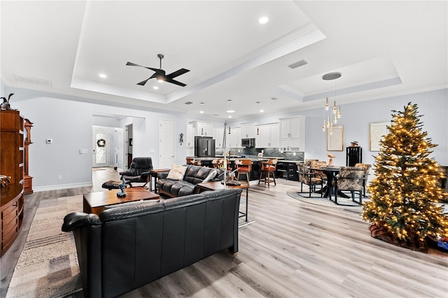 living room with ceiling fan, crown molding, light hardwood / wood-style flooring, and a tray ceiling