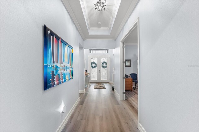 corridor with a raised ceiling, french doors, crown molding, and light hardwood / wood-style flooring