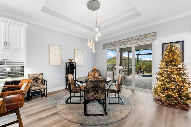 dining area with a tray ceiling, light hardwood / wood-style flooring, and crown molding