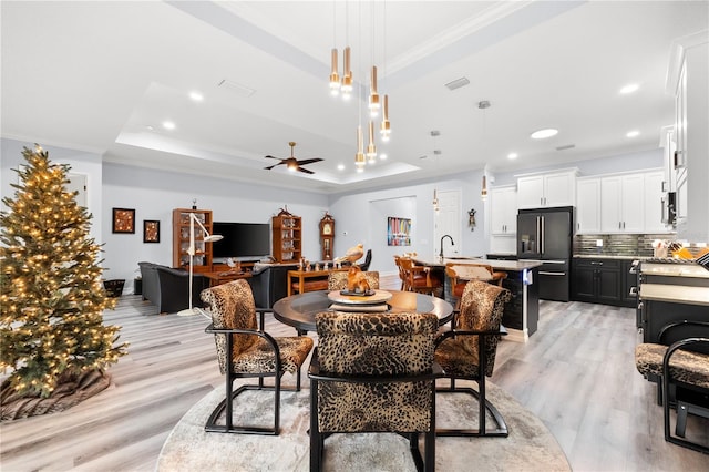 dining area featuring a raised ceiling, ceiling fan, ornamental molding, and light wood-type flooring