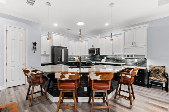 kitchen with a breakfast bar, a center island with sink, decorative light fixtures, white cabinetry, and stainless steel appliances