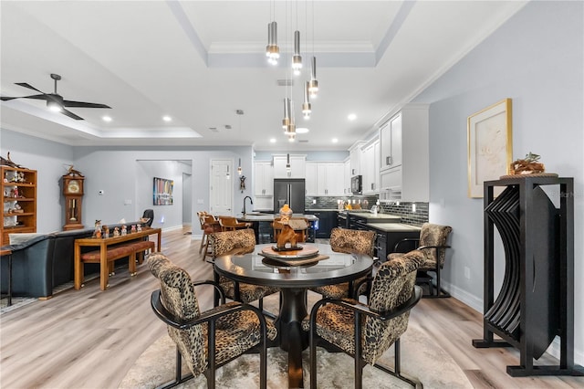 dining space featuring ceiling fan, light wood-type flooring, and a tray ceiling